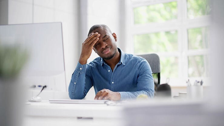 Stressed and frustrated employee rubs his forehead at his desk